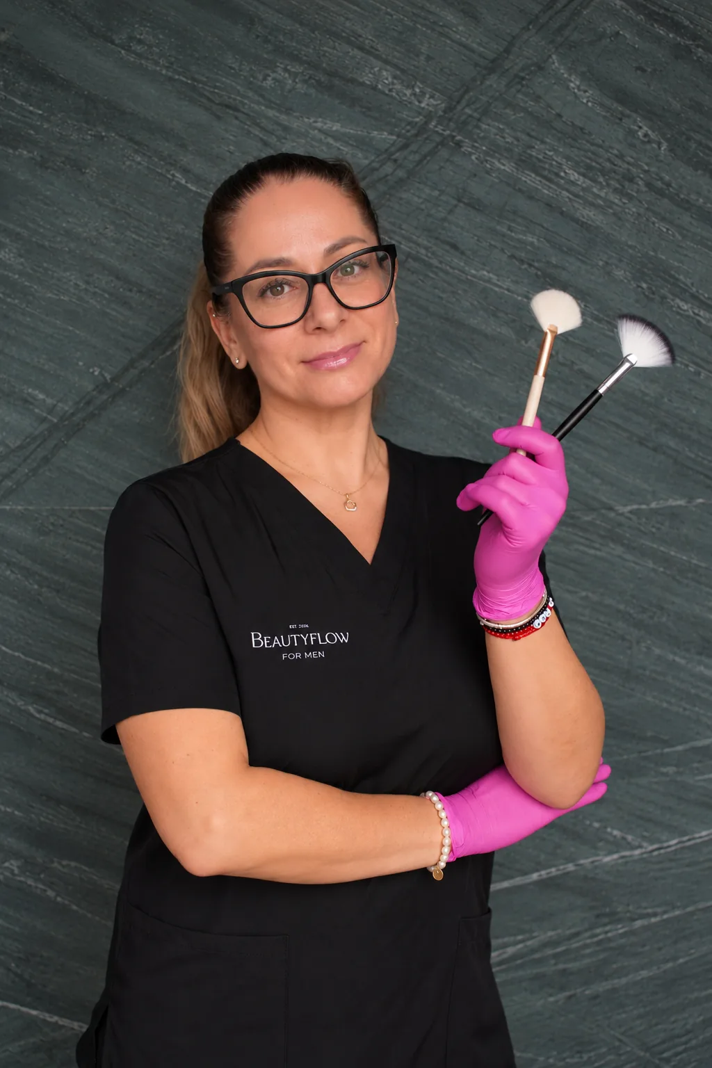Brigi, die Kosmetikerin von Beautyflow for Men, mit zwei Kosmetikpinseln in der Hand